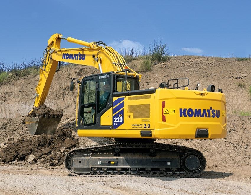 Yellow Komatsu excavator digging soil at a construction site with a blue sky above.
