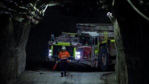 1782246436_63866_en_e6d5b_66001_unsplash-40-under-40-site-mediajpg - Machines Wiki Worker in orange safety vest and helmet directing a large dump truck through a dark underground mine passage.