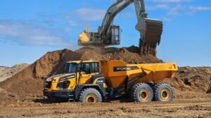 Yellow Hyundai excavator dumps dirt onto a large mound while a Hyundai articulated dump truck waits nearby at a construction site.