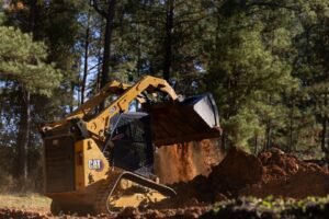 Yellow CAT excavator dumping soil into a pile in a pine forest clearing. (informative)