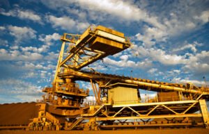 Port-Hedland-iron-ore-stackerjpg - Machines Wiki Massive yellow mining conveyor system with walkways against a bright blue sky.