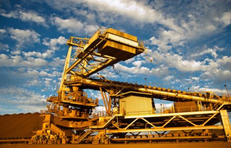 Port-Hedland-iron-ore-stackerjpg - Machines Wiki Massive yellow mining conveyor system with walkways against a bright blue sky.