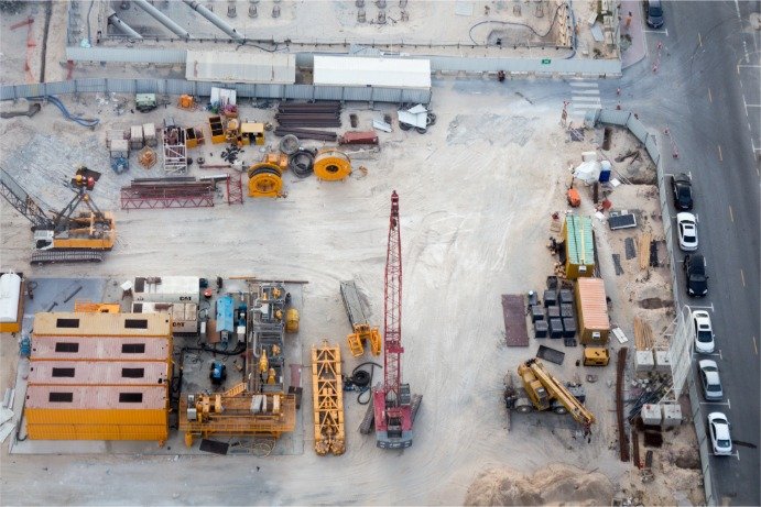 CECE Formalises a Strategic Partnership with DLL Aerial view of an active construction site with a red crane, yellow machines, and stacked materials near a street on the right side.