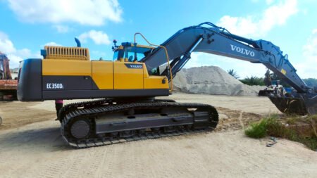 Yellow Volvo EC350D L excavator on tracks at a dirt construction site with a large pile of soil and blue sky behind it