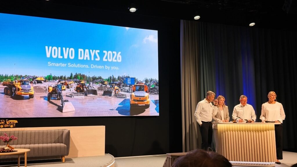 Stage presentation with a large screen reading 'VOLVO DAYS 2026' showing construction equipment; five people in white at a podium/table on the right.