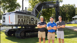 1783371882_63961_en_63c80_66112_john-deere-building-americapng - Machines Wiki Three men pose in front of a large John Deere excavator with the words 'BUILDING AMERICA' on the machine, outdoors on a sunny day.