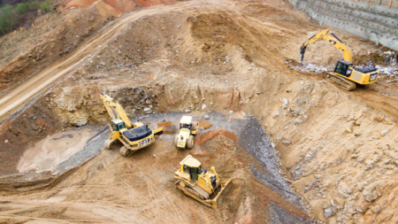 1783450146_63966_en_ddc59_66119_unsplash-cat-surface-miningpng - Machines Wiki Wide shot of a construction site with multiple yellow Caterpillar excavators and a bulldozer working in a terraced dirt pit.