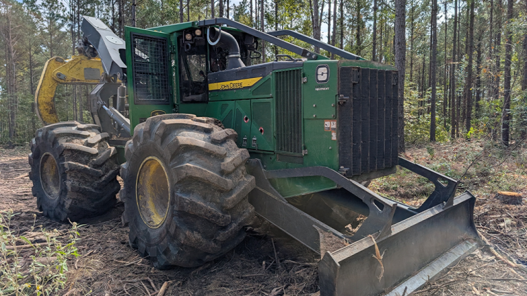 Titan expands offerings for rugged terrain with new ForestEDGE tire lineup Green John Deere forestry harvester with oversized tires and a front blade in a pine forest clearing.