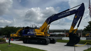 Large blue and yellow Komatsu excavator on display outdoors with another machine in the background near a white tent.