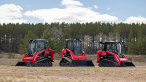 1784328027_64021_en_d2311_66188_yanmar-ctl-posi-trackpng - Machines Wiki Three red compact track loaders with wide buckets lined up on a dirt field, with a pine forest in the background.