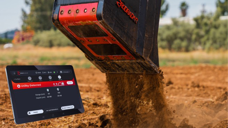 1784829579_64049_en_4d43b_66229_rod-radar-bucket-utility-detectionpng - Machines Wiki Excavator bucket dumping dirt at a construction site; a tablet shows a monitoring app with a 'Utility Detected' alert.