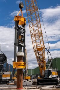 Large yellow Liebherr crane and drilling rig at a construction site under a blue sky with scattered clouds