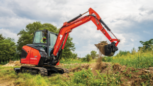 Orange compact excavator digging soil in a grassy field, bucket raised to scoop dirt