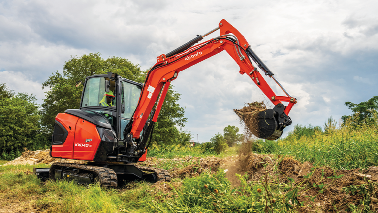 Orange compact excavator digging soil in a grassy field, bucket raised to scoop dirt