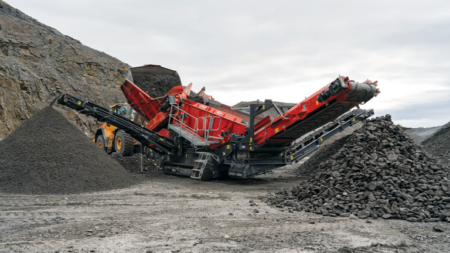 Industrial rock crusher and conveyor system at a quarry, processing stone into gravel with piles of crushed rock nearby