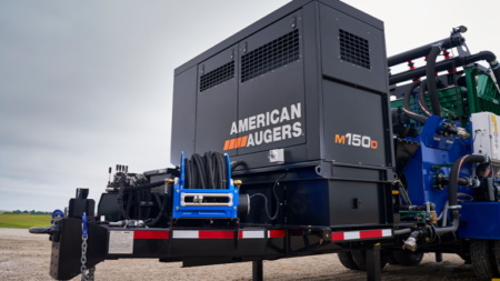 Industrial drilling rig on a trailer outdoors, with 'American Augers' logo visible on the black enclosure (M1500D).