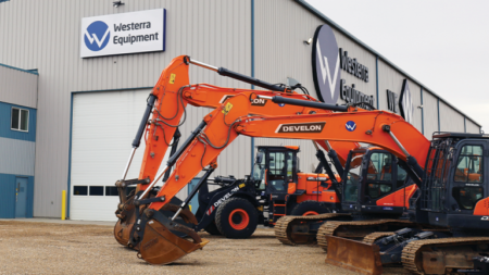 Large orange excavator with bucket attached, parked in a yard outside a Westerra Equipment building