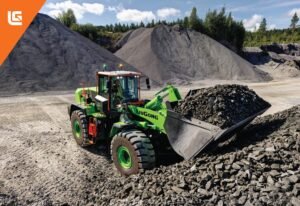 Green Liugong wheel loader at a gravel quarry beside large mounds of rock under a blue sky with trees in the background (orange corner banner).