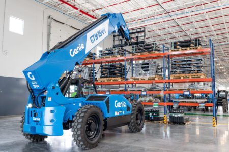 Blue Genie GTH-1544 telescopic boom lift inside a warehouse with tall orange and blue storage racks and pallets nearby, ready for use.