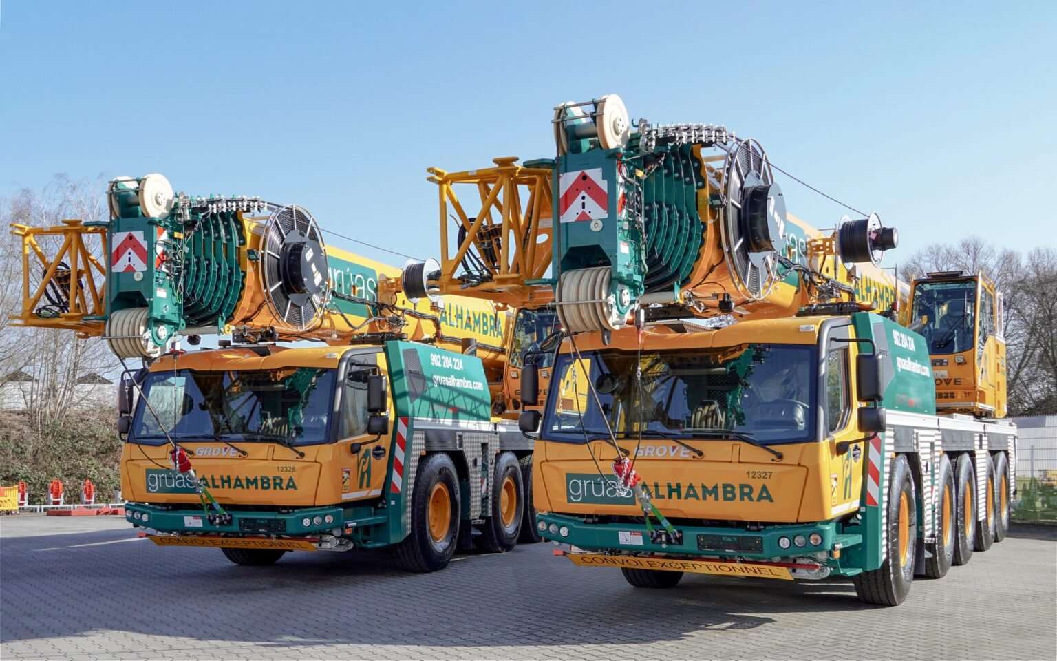 Gruas-Alhambra-adds-new-Grove-GMK5120L-cranes-at-SMOPYC-2026-01-scaledjpg - Machines Wiki Two large mobile crane trucks parked side by side, with reels, cables, and machinery mounted on their yellow and teal frames against a clear blue sky.