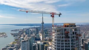 Image-Credit-Justin-McConnell-Terex-CTT-472-flat-top-drives-construction-of-Canadas-tallest-residentjpeg - Machines Wiki Crane atop a high-rise under construction overlooking a city with a waterfront and the CN Tower in the distance.