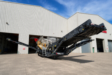 MAGNA_MT6Spng - Machines Wiki Large mobile conveyor belt system with long extended arms parked outside a metal warehouse