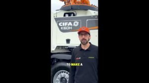 maxresdefault-1jpg - Machines Wiki Presenter in a black polo with CIFA and Zoomlion logos stands in front of a large white CIFA K60H concrete mixer truck, wearing an orange cap with a logo.