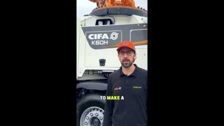 maxresdefault-1jpg - Machines Wiki Presenter in a black polo with CIFA and Zoomlion logos stands in front of a large white CIFA K60H concrete mixer truck, wearing an orange cap with a logo.