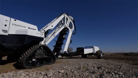 White excavator with a long articulated arm and tracked undercarriage on a rocky construction site under a clear blue sky