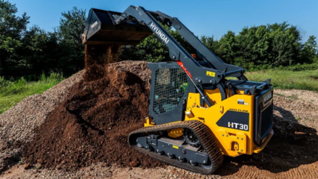 1785883854_64137_en_69074_66317_hyundai-ht30-ctlpng - Machines Wiki Hyundai HT30 compact tracked loader dumping dirt onto a large mound at a construction site.