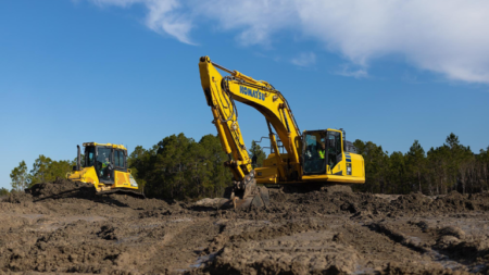 1785955286_64141_en_3e2f8_66321_komatsu-smart-construction-aim-intelligent-machinespng - Machines Wiki Two yellow excavators work on a dirt construction site under a clear blue sky, one actively digging while the other rests nearby.
