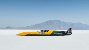 1786127870_64158_en_284ac_66343_jcb-hydromax-2png - Machines Wiki Jet-powered land speed car on a salt flat with mountains in the background, painted yellow, black, and green with JCB branding (Hydro MAX)
