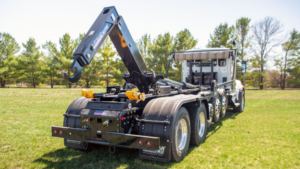 Heavy-duty tow truck with a hydraulic crane and hook, parked on a grassy field with trees in the background.