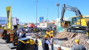 Outdoor construction equipment expo with a large yellow Hyundai excavator on a rocky display and visitors nearby