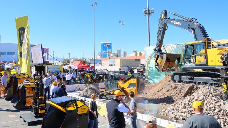1787000392_63867_en_9985e_66002_conexpo-earthmoving-roundupjpg - Machines Wiki Outdoor construction equipment expo with a large yellow Hyundai excavator on a rocky display and visitors nearby
