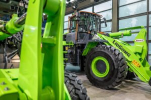 LG_Ecomondo_2024_003jpg - Machines Wiki Green LiuGong wheel loader on display in a showroom, large front bucket raised, showcasing industrial machinery details.