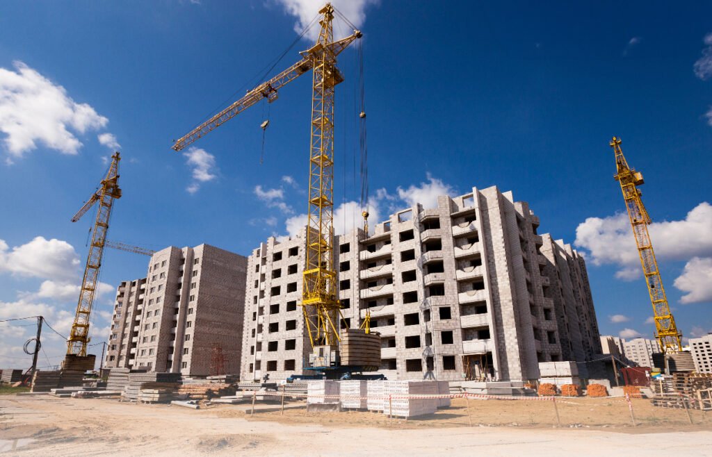 Construction site with a tall yellow crane over an unfinished multi-story concrete building against a blue sky.
