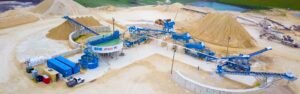 A sand mining and processing facility with blue conveyor belts, processing equipment, and large piles of sand.