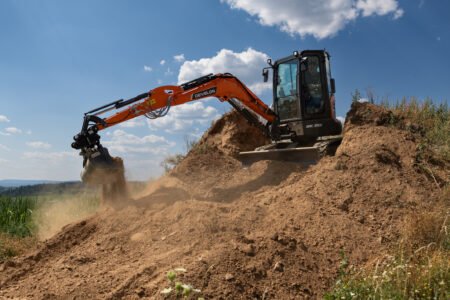 Y2A3079_redjpg - Machines Wiki Orange excavator with hydraulic arm digging a dirt hill under a blue sky